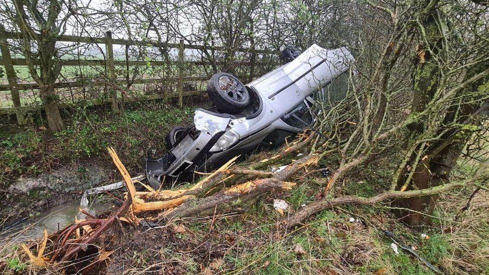 A crashed car upside down in a ditch on the A1307 close to Godmanchester