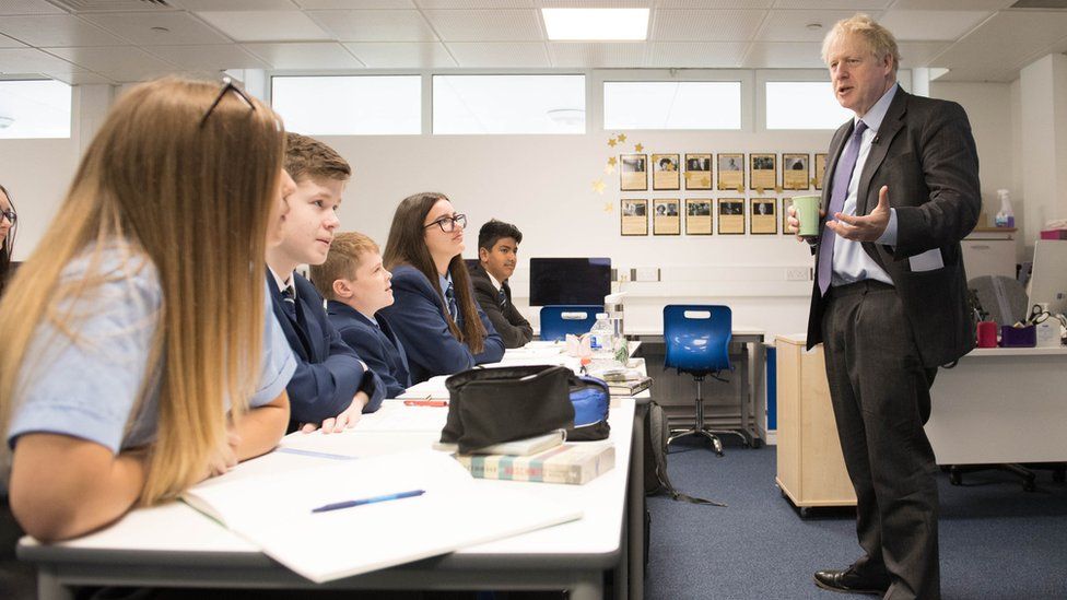 Boris Johnson holds a cup of coffee while speaking in front of a class of students