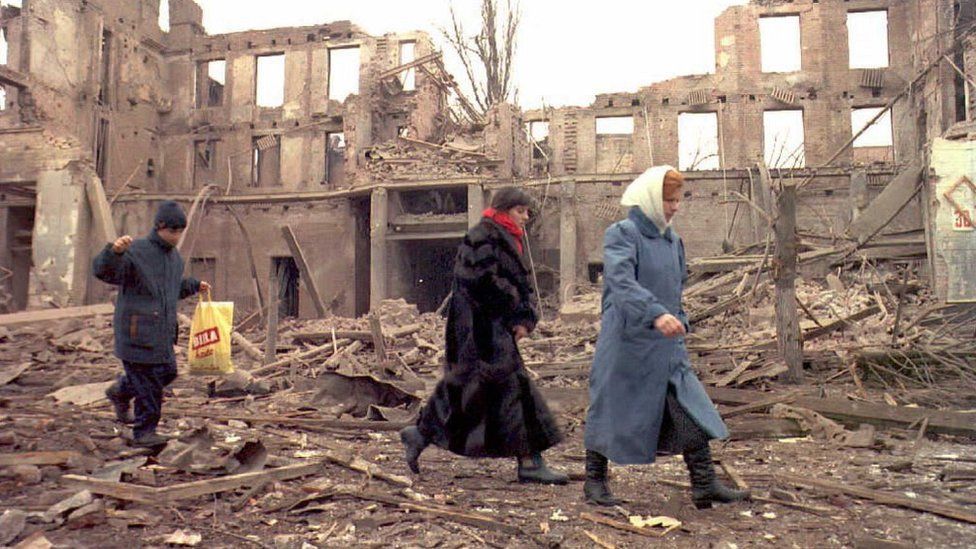 Chechen civilians walk past the remains of buildings in Grozny