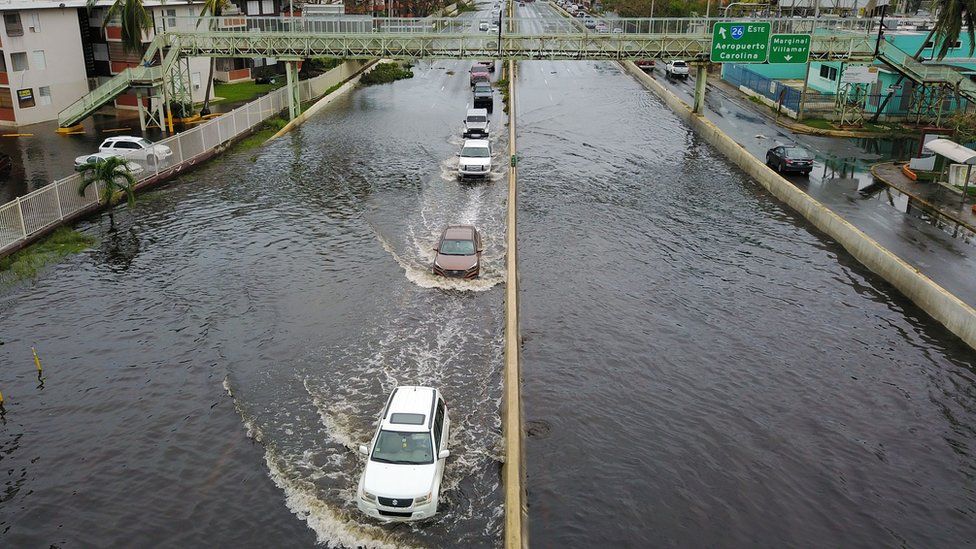 Image shows cars driving through a flooded road in the aftermath of Hurricane Maria in San Juan, Puerto Rico on 21 September 2017