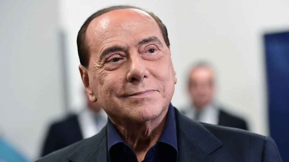 Silvio Berlusconi smirks, looking confident, at a polling station after casting his vote