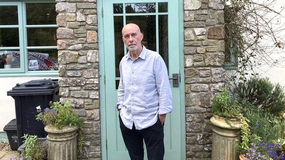 Ian Scott standing by the front door to a house
