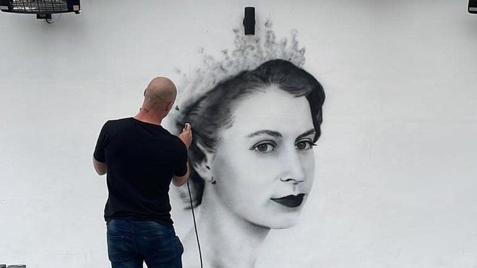 Street artist painting a mural of the Queen