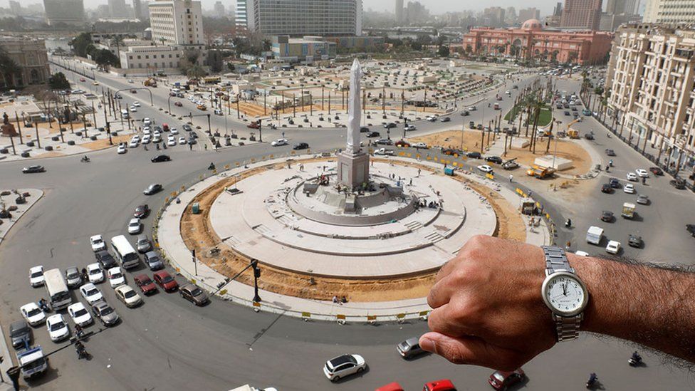 A wristwatch showing noon with Tahrir Square, Cairo, in the background