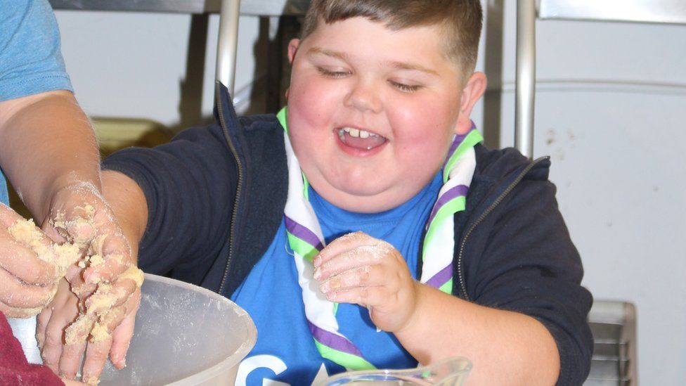 A boy dipping his hand in a cake mixture bowl