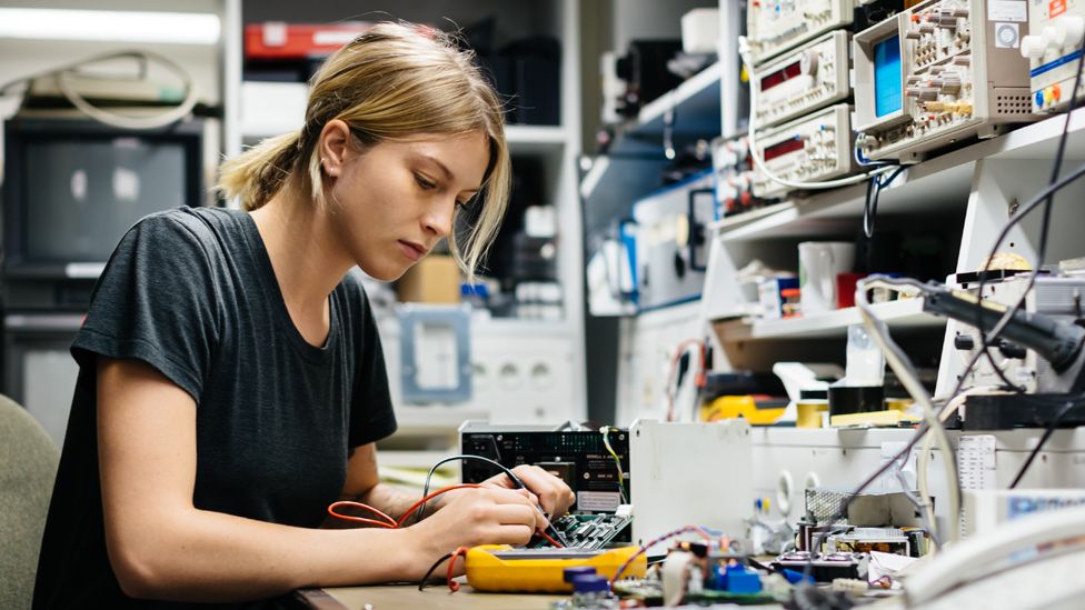 Молодая женщина-инженер измеряет напряжение на проводнике в своей мастерской