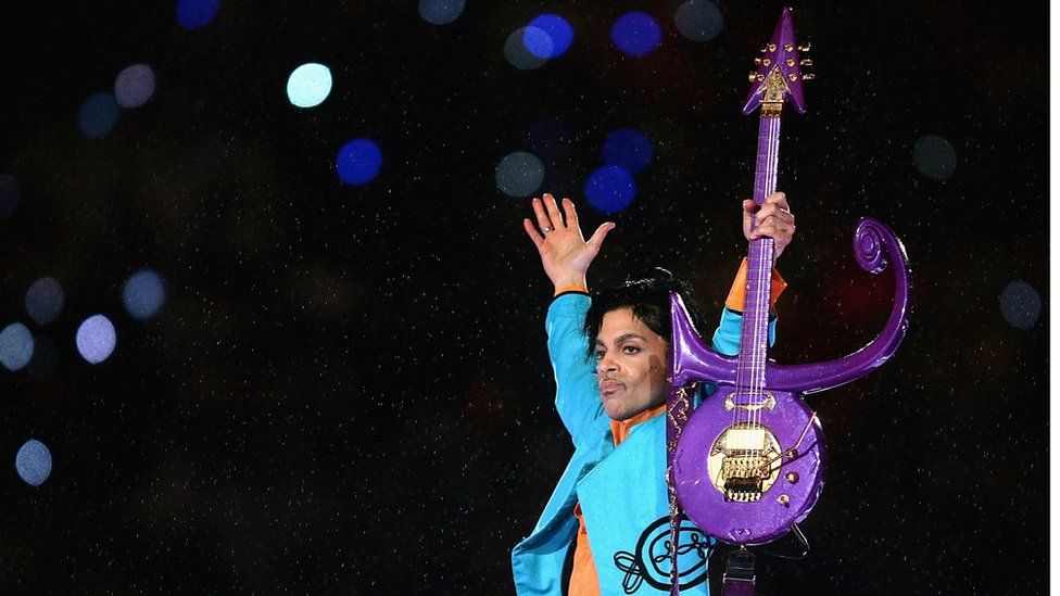 Prince holds a guitar shaped like the symbol that he took as his name in 1993
