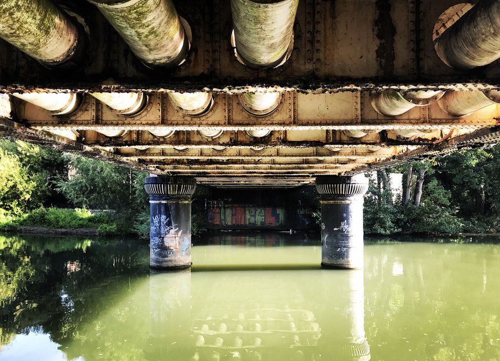 A bridge covered in graffiti sit over a green canal