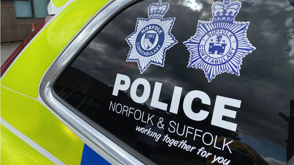 A police car with the badges for both Norfolk and Suffolk police forces on the window