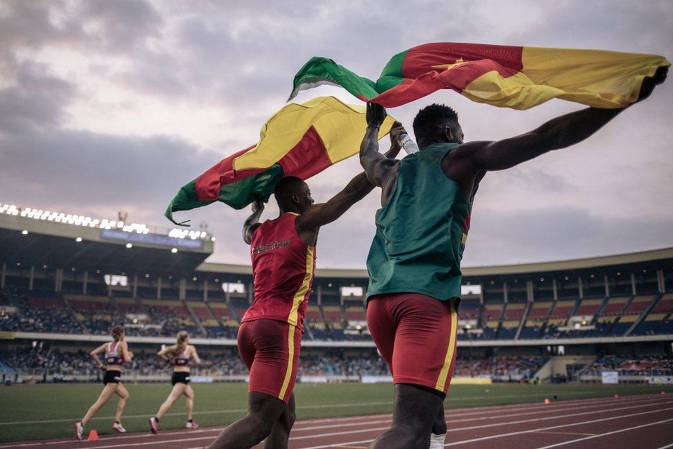 Two men holding Cameroon flag at sport stadium, 1 August 2023