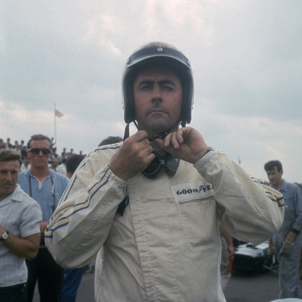 Australian racing driver Jack Brabham fastening his helmet at Silverstone, July 1967, the year that Brabham team won their second consecutive constructors championship.