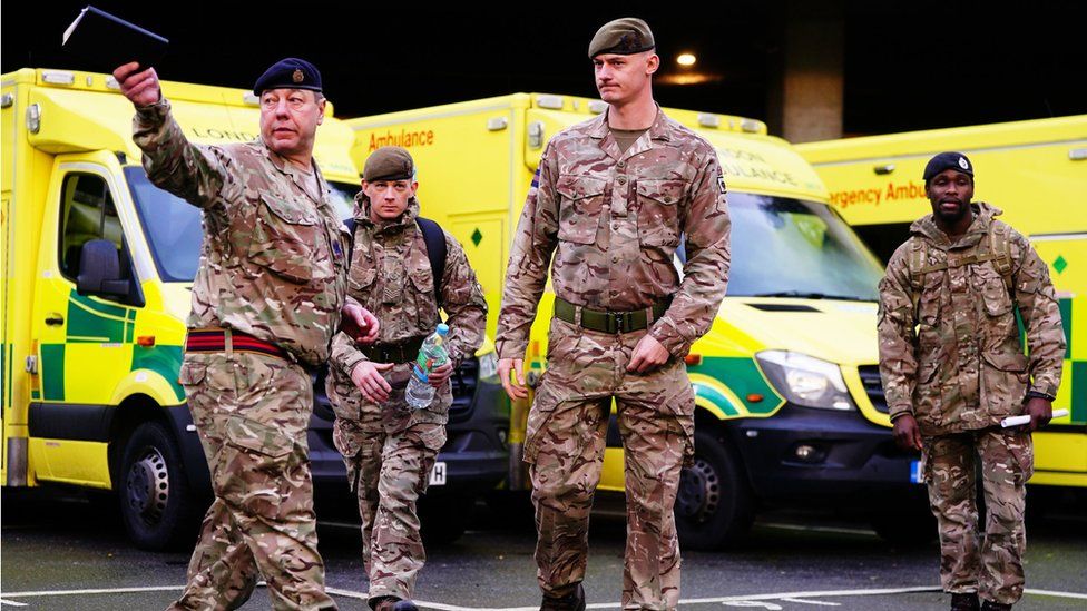 Military personnel stand in front of ambulances being briefed.