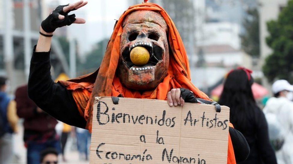 A person in a costume carries a poster against the so-called "Orange Economy"