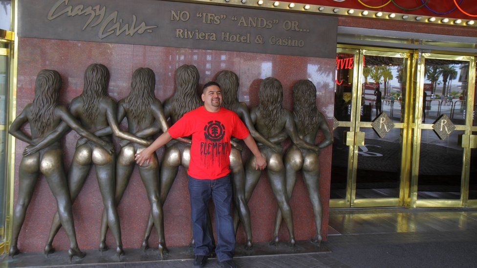 A man poses with bronze statues showing Crazy Girls