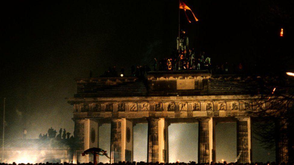 Revellers at the Brandenburg Gate stand on top of a remnant of the Berlin Wall, as they celebrate the first New Year in a unified Berlin since World War II on 31 December 1989