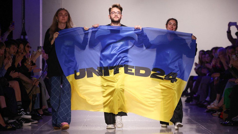 Ukrainian fashion designers Ksenia Schnaider, Ivan Frolov and Julie Paskal walk the catwalk with a Ukraine flag, following the "Ukraine Fashion Week presents: FROLOV, KSENIASCHNAIDER, PASKAL" show during London Fashion Week, in London, Britain, February 21, 2023.