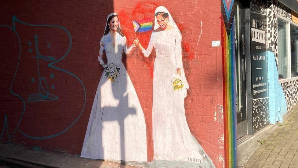 A street art painting of Kate Middleton and Meghan Markle wearing wedding dresses and waving a LGBTQ flag