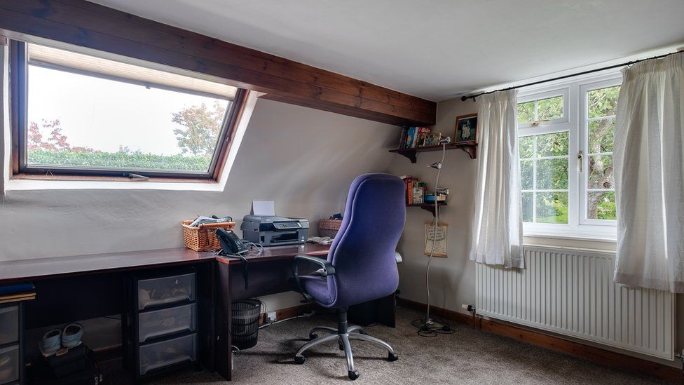 An image of an attic study room with a blue chair at a deep brown desk.