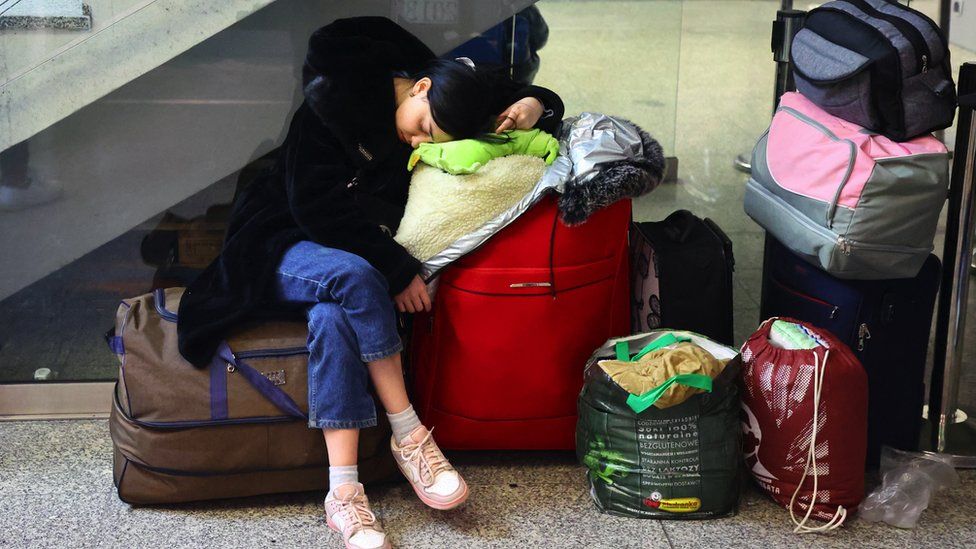 Woman sleeps on her luggage in a train station in Krakow, Poland