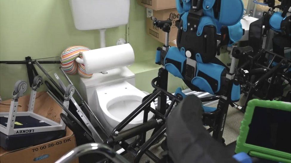 Wheelchairs and equipment surround a toilet area