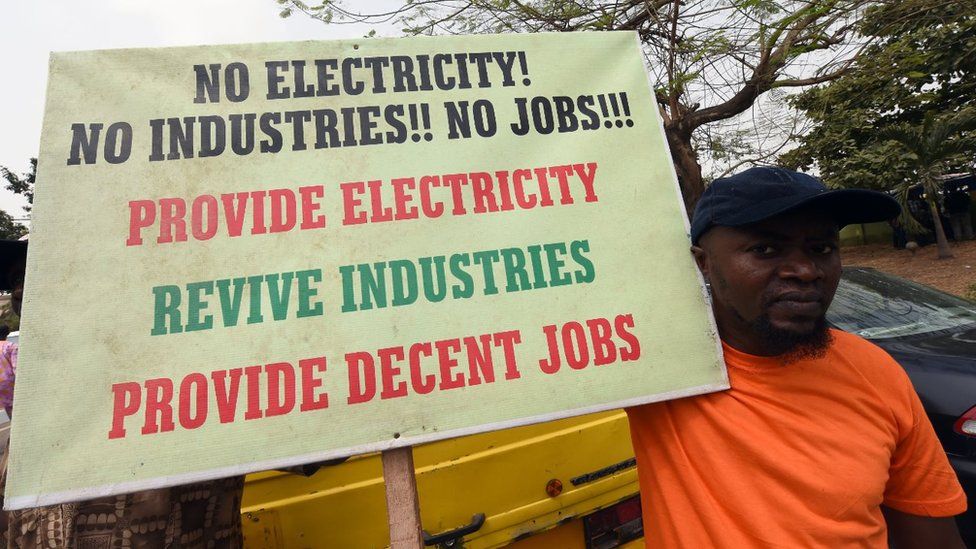 Мужчина держит плакат с надписью «Нет электричества!» Никаких производств!! Нет работы!!! Обеспечьте электроэнергией, оживите промышленность, обеспечьте достойные рабочие места» во время демонстрации протеста против 45-процентного повышения цен на электроэнергию 8 февраля 2016 года в Лагосе.