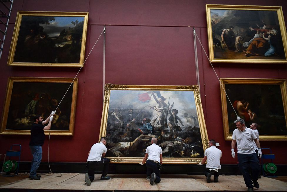 Workers hang Eugene Delacroix's painting "Liberty Guiding the People" marking its return at the Louvre Museum in Paris on April 30, 2024.