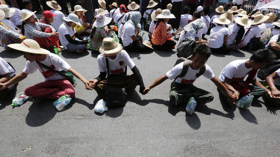Protesters sitting on a road join hands as they demand labour rights