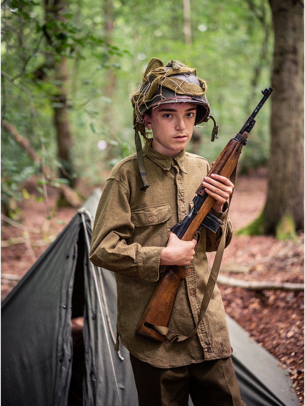 A boy stands in the woods dressed as a solider from World War Two