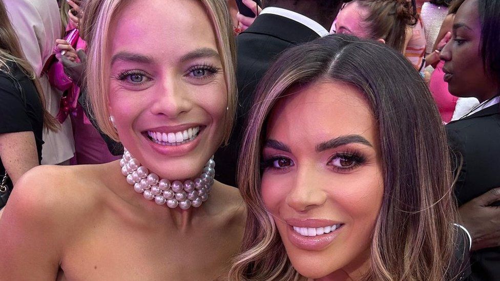Ekin-Su Cülcüloğlu and Margot Robbie smiling for a selfie at the Barbie premiere in London. Margot has a pearl necklace on and has her blonde hair tied up while Ekin-Su has her brunette hair down
