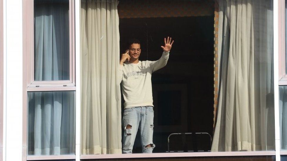Roger Goncalves, who is from Brazil and travelled via Madrid to get to the UK, waves to members of the media from the window of Radisson Blu Edwardian Hotel, near Heathrow Airport, London