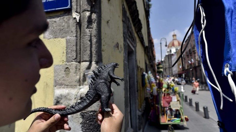 A fan holds a Godzilla plastic toy while watching the shooting of scenes of the movie "Godzilla, King of the Monsters" in the historical centre of Mexico City on August 20, 2017.