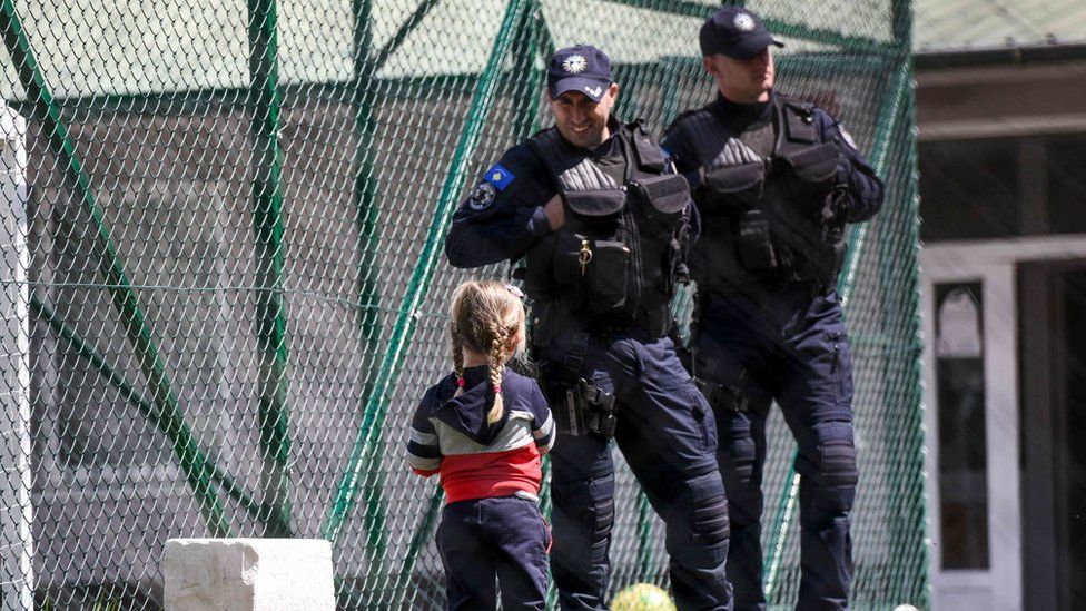 Image shows a young Kosovar child looking at Kosovar police officers