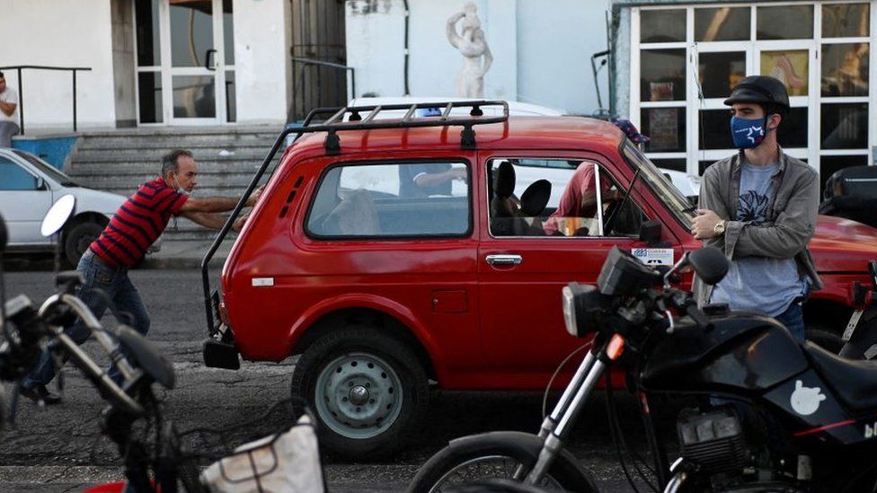 Мужчина стоит перед красной машиной, которую толкают двое других мужчин в Гаване, 22 марта 2022 г.