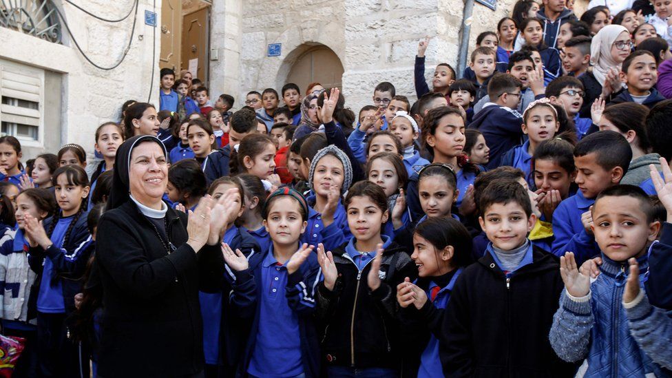 Монахиня хлопает в ладоши с палестинскими школьниками в ожидании возвращения реликвии в Вифлееме, 30 ноября 2019 г.