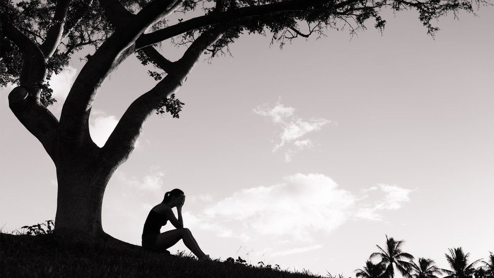 A silhouette of a woman sitting under a tree