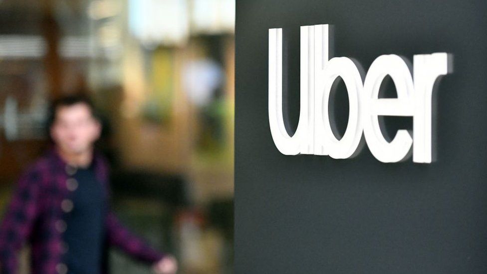 An Uber logo is seen on a sign outside the company's headquarters location as people protest nearby in San Francisco