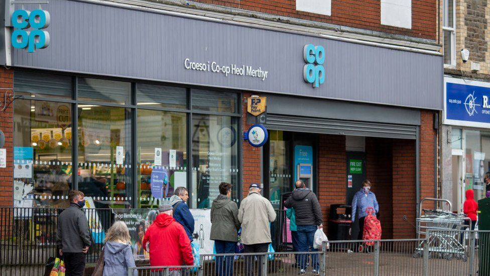 Customers queue outside a Co-op convenience store in Cardiff, Wales