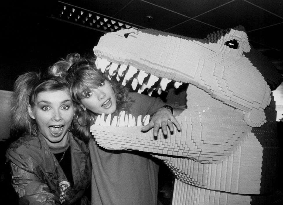 Two singers pose with a Lego dinosaur