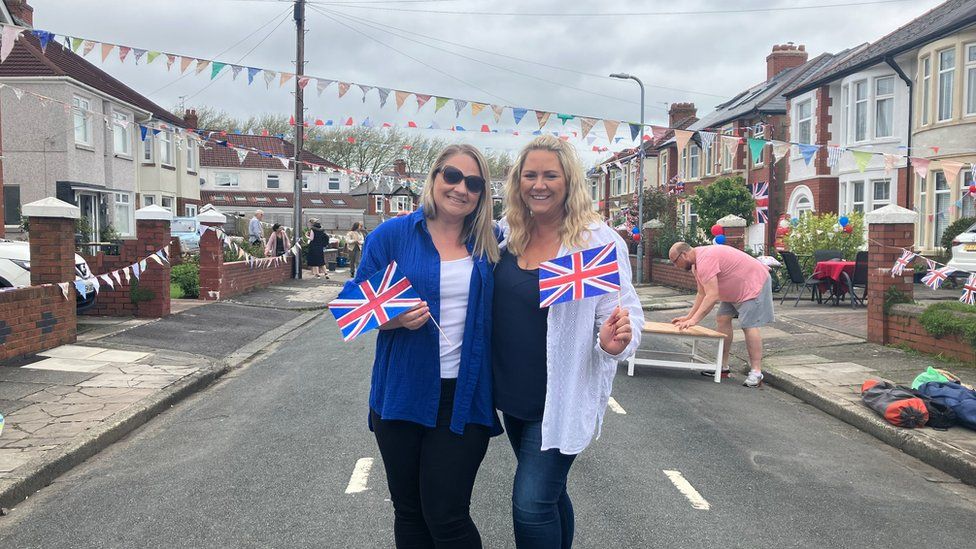 two women holding union jacks on a street with bunting