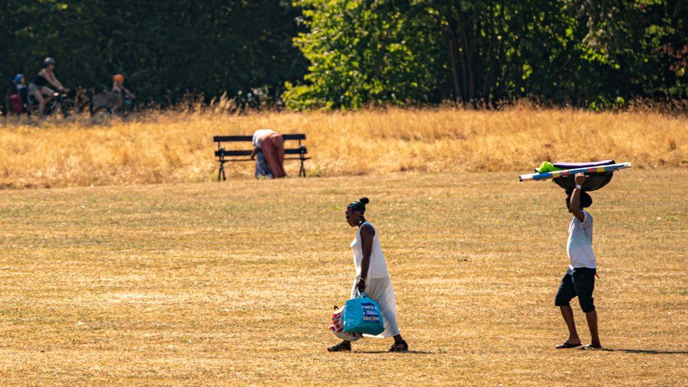 People walk over parched grass in Eastville Park, Bristol.