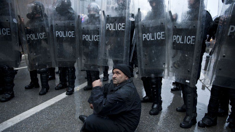 A man sits in front of a cordon of policemen in riot gear during the demonstration