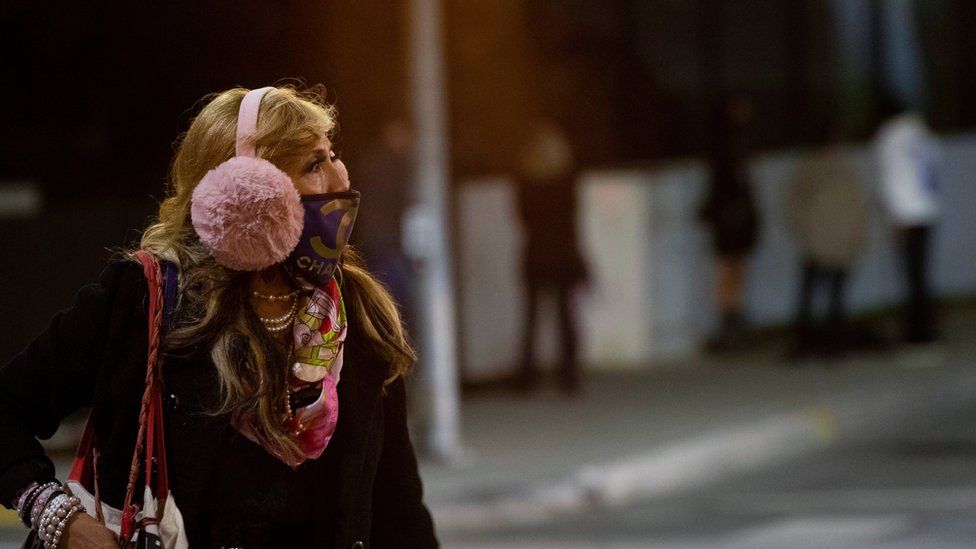 A woman wearing a protective face mask and earmuffs crosses the street during the outbreak of the coronavirus disease) in Beverly Hills, California, US, November 20, 2020