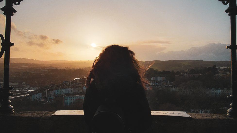 A woman looks out over Bristol from Cabot Tower in Brandon Hill Park. It is dusk