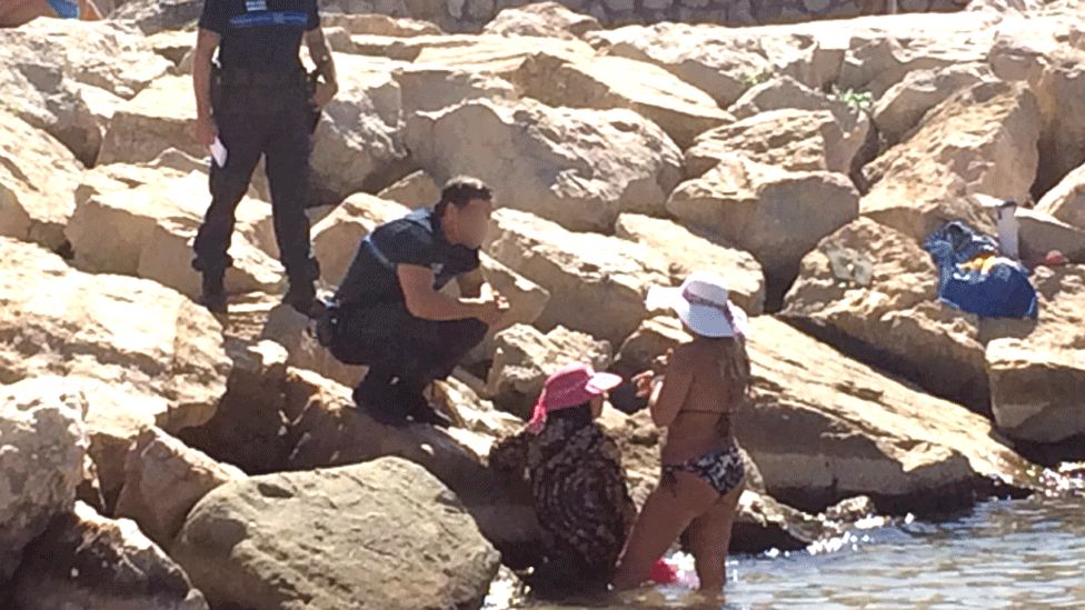 A woman (in pink hat) is given a fine on the beach at Cannes on Monday