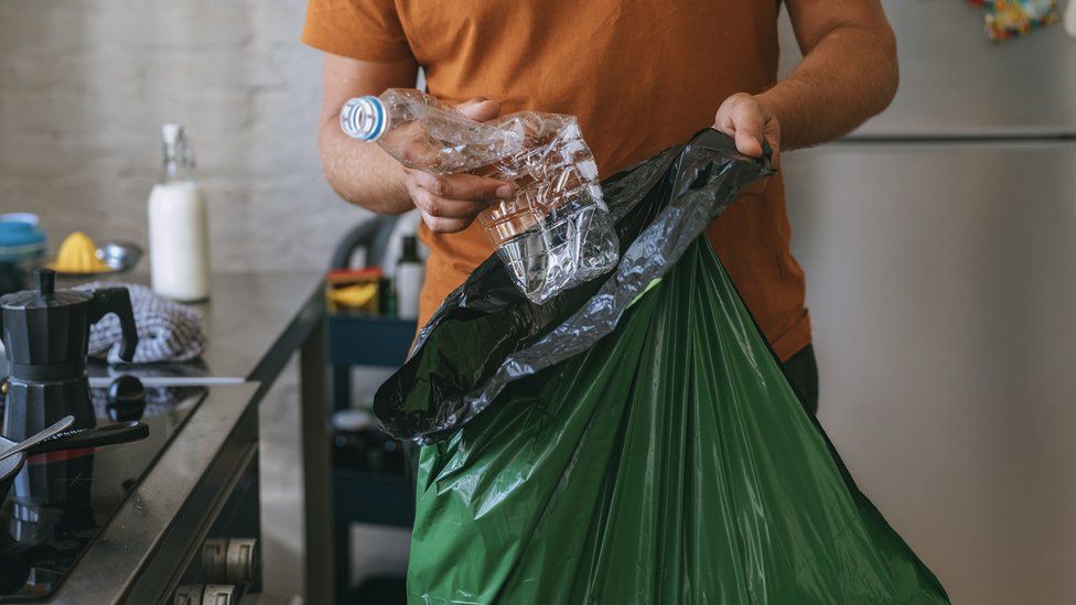 man places plastic bottle in bin bag