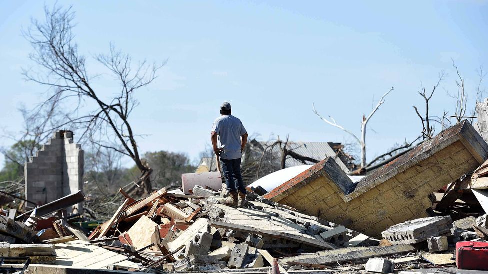 A photo of a man standing on top of rubble of a home flattened by the tornado