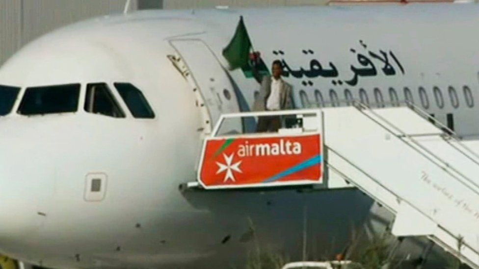 An Afriqiyah Airways plane stands on the tarmac at Malta International airport as an unidentified man waves a flag