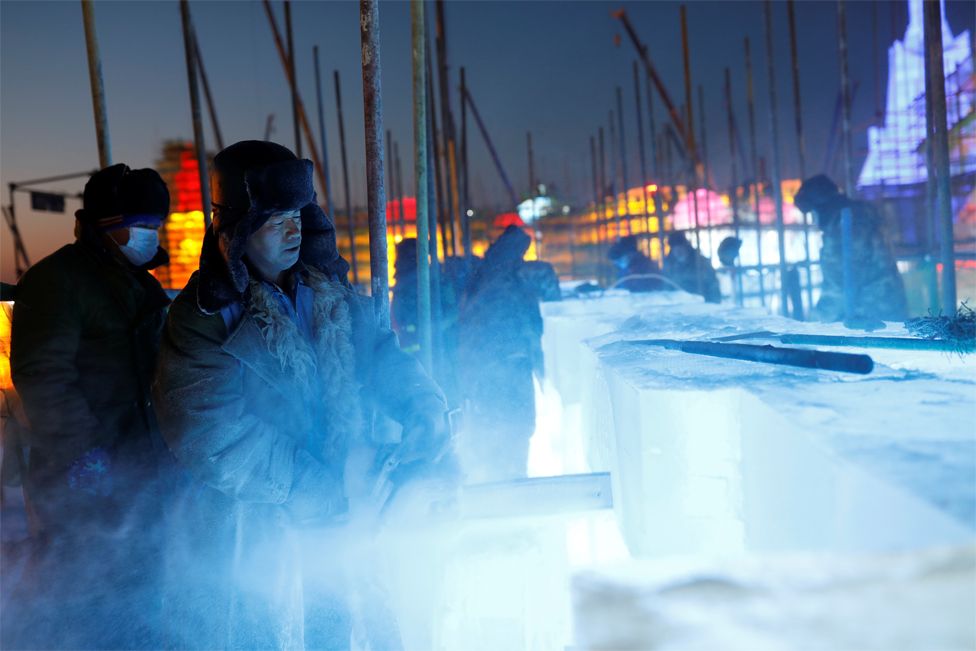 A worker uses a chainsaw to carve a block of ice