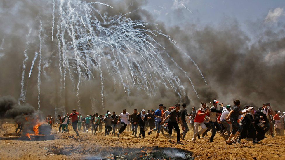 Gazans run for cover from tear gas during clashes with Israeli security forces near the Israeli border fence, 14 May 2018