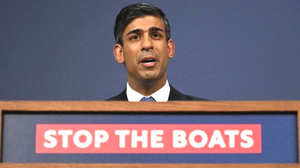 Rishi Sunak speaking from a podium reading "stop the boats"